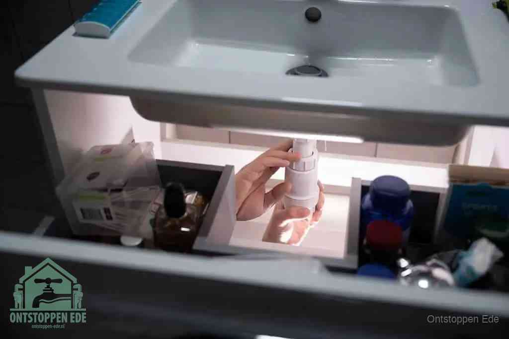Een pompfles met zeep boven een wastafel, de heet water en afwasmiddel-methode om een vetprop in de afvoer los te maken in Ede