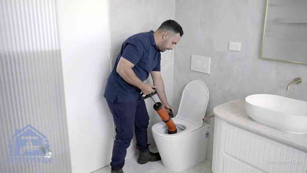Een monteur buigt over een wandcloset en duwt met de hand een persluchtontstopper in de toiletpot om de verstopping handmatig los te maken in Ede