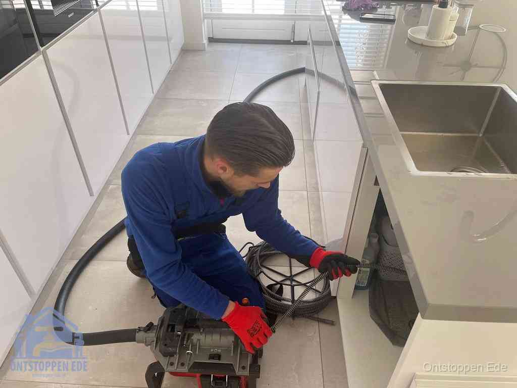 Een monteur ontstopt de keukenafvoer onder de spoelbak met een elektrische veermachine in Ede