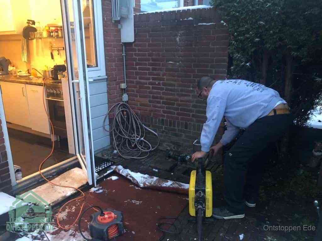 Een monteur werkt buiten bij een open riool-/grondput met een elektrische ontstoppingsmachine om een verborgen afvoerprobleem op te sporen in Ede