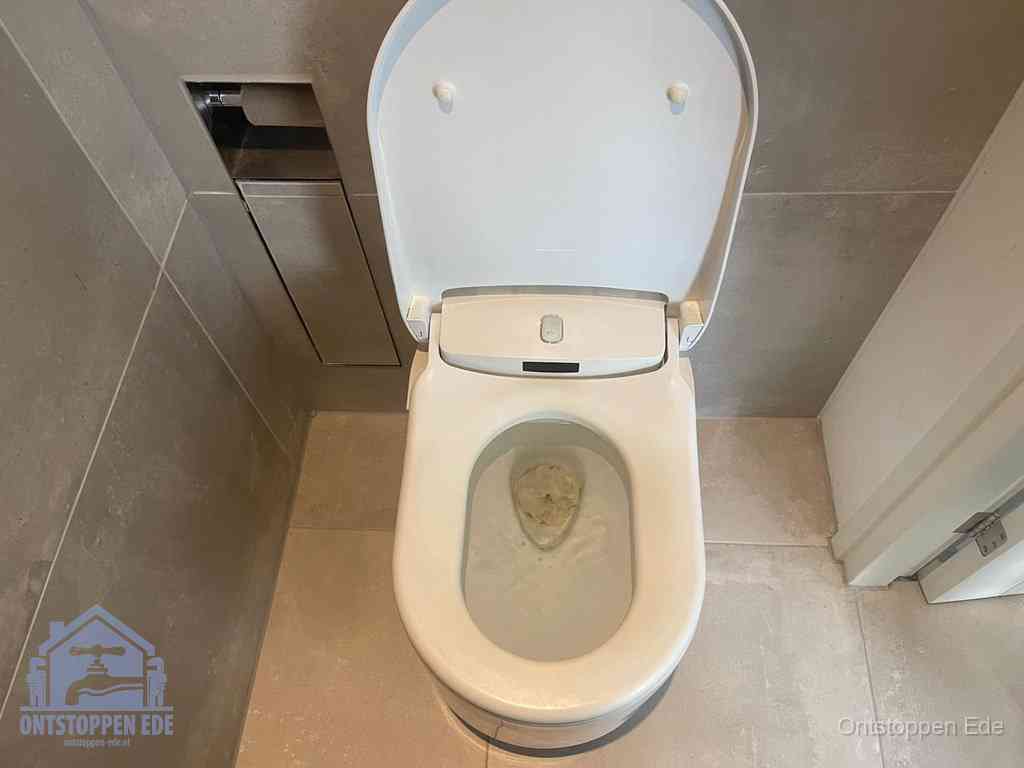 Een wit hangtoilet waarin een prop wc-papier op het water blijft drijven, een duidelijk signaal van een verstopte wc in Ede