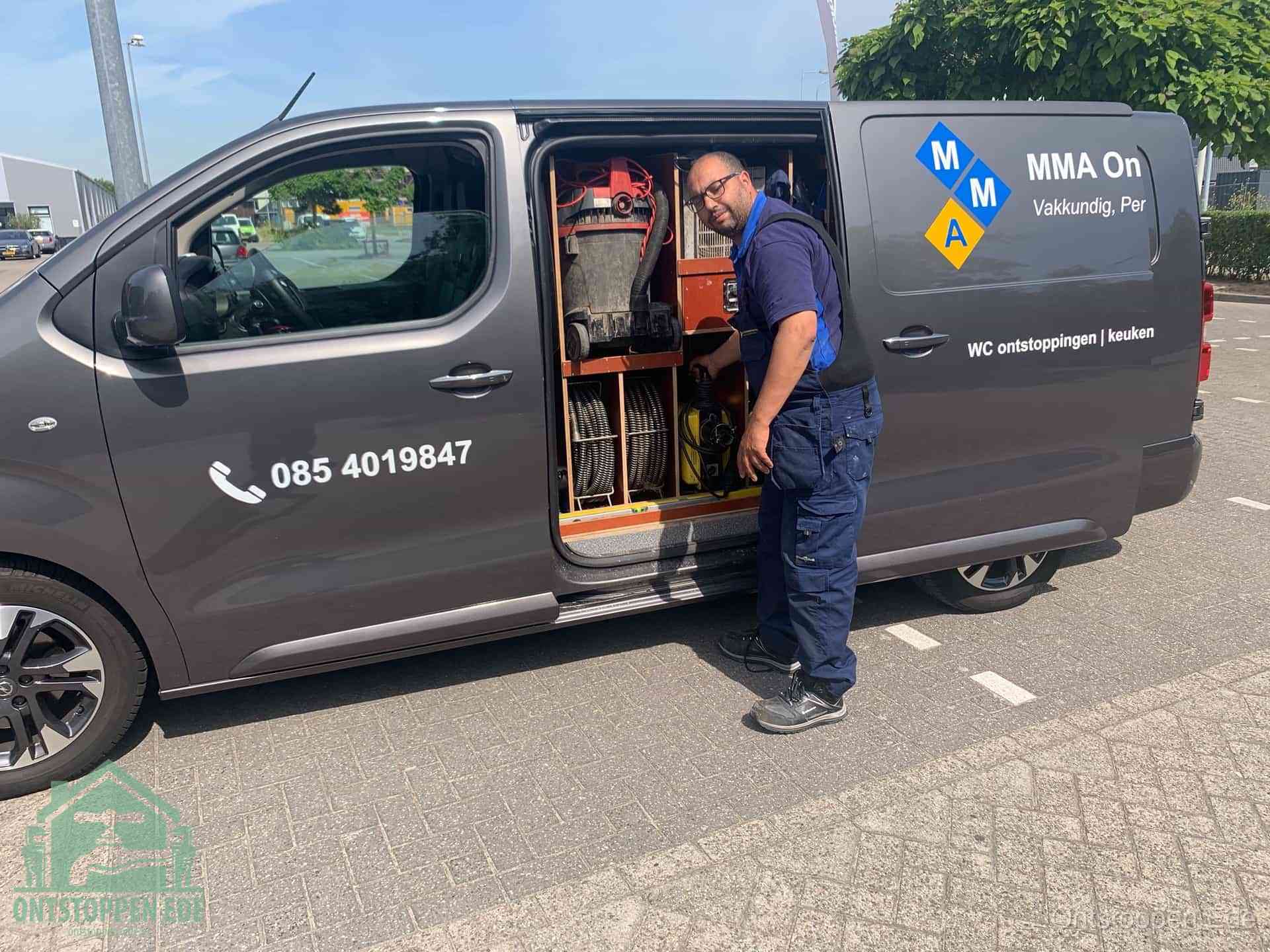 Een monteur bij de open schuifdeur van zijn bedrijfsbus op een parkeerplaats, klaar om de oorzaak van terugkerende afvoerverstoppingen aan te pakken in Ede