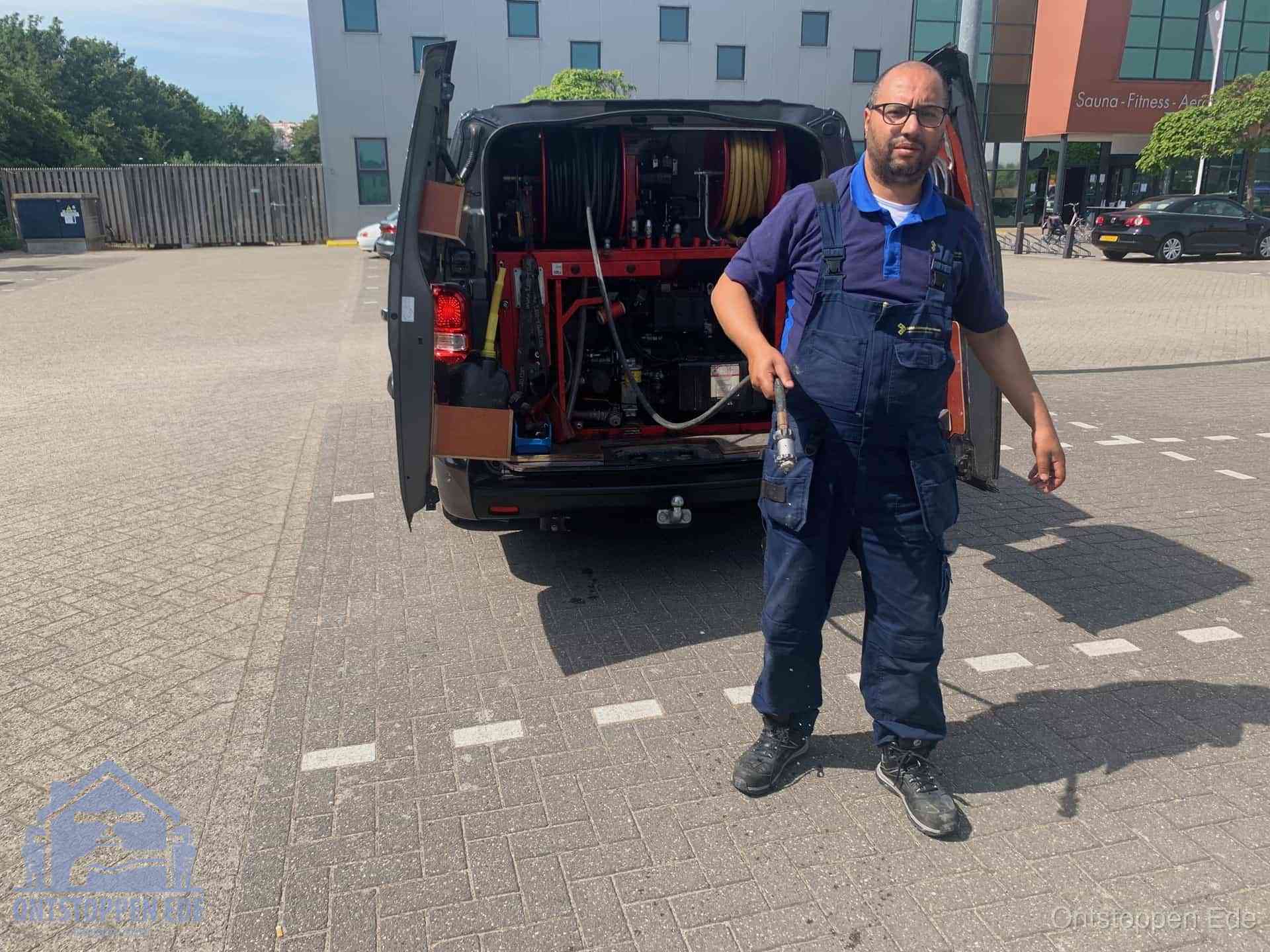Een monteur bij zijn bestelbus met een hogedruk- en rioolreinigingsunit, klaar om de oorzaak van terugkerende wc-verstoppingen aan te pakken in Ede