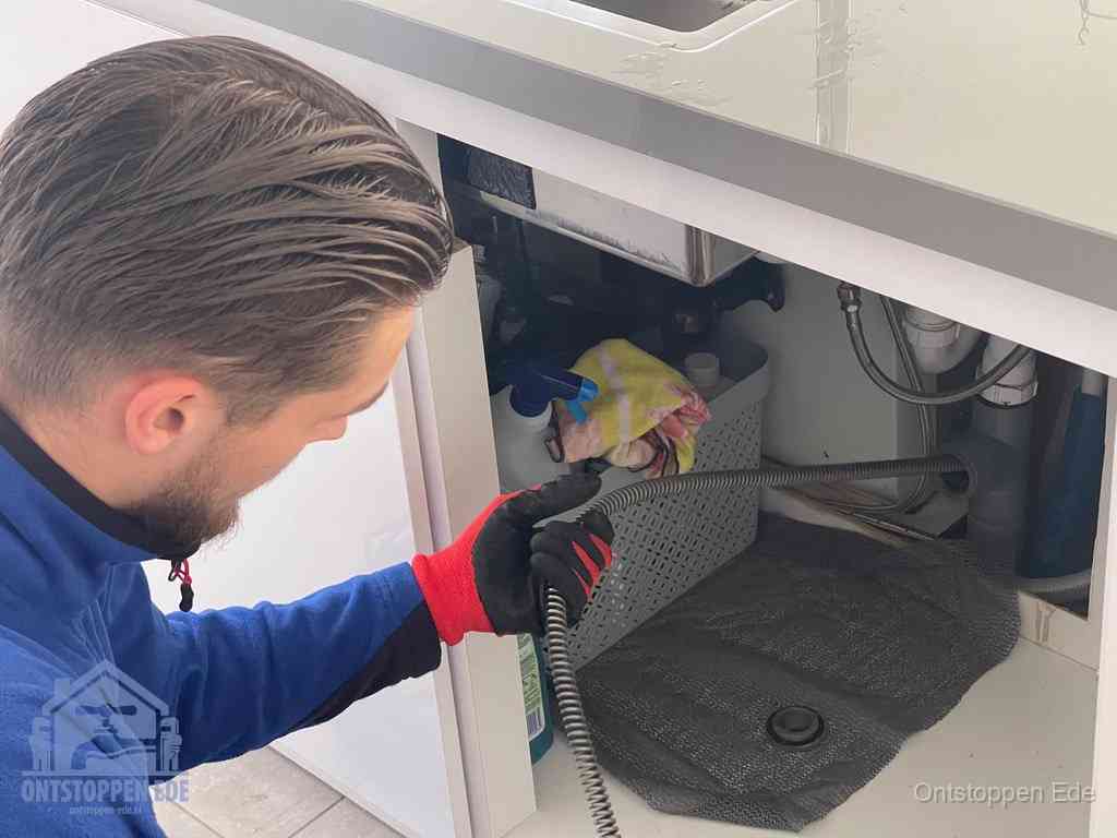Een monteur voert een flexibele ontstoppingsveer in de afvoer om een verstopping voorbij de bocht van het toilet te bereiken in Ede